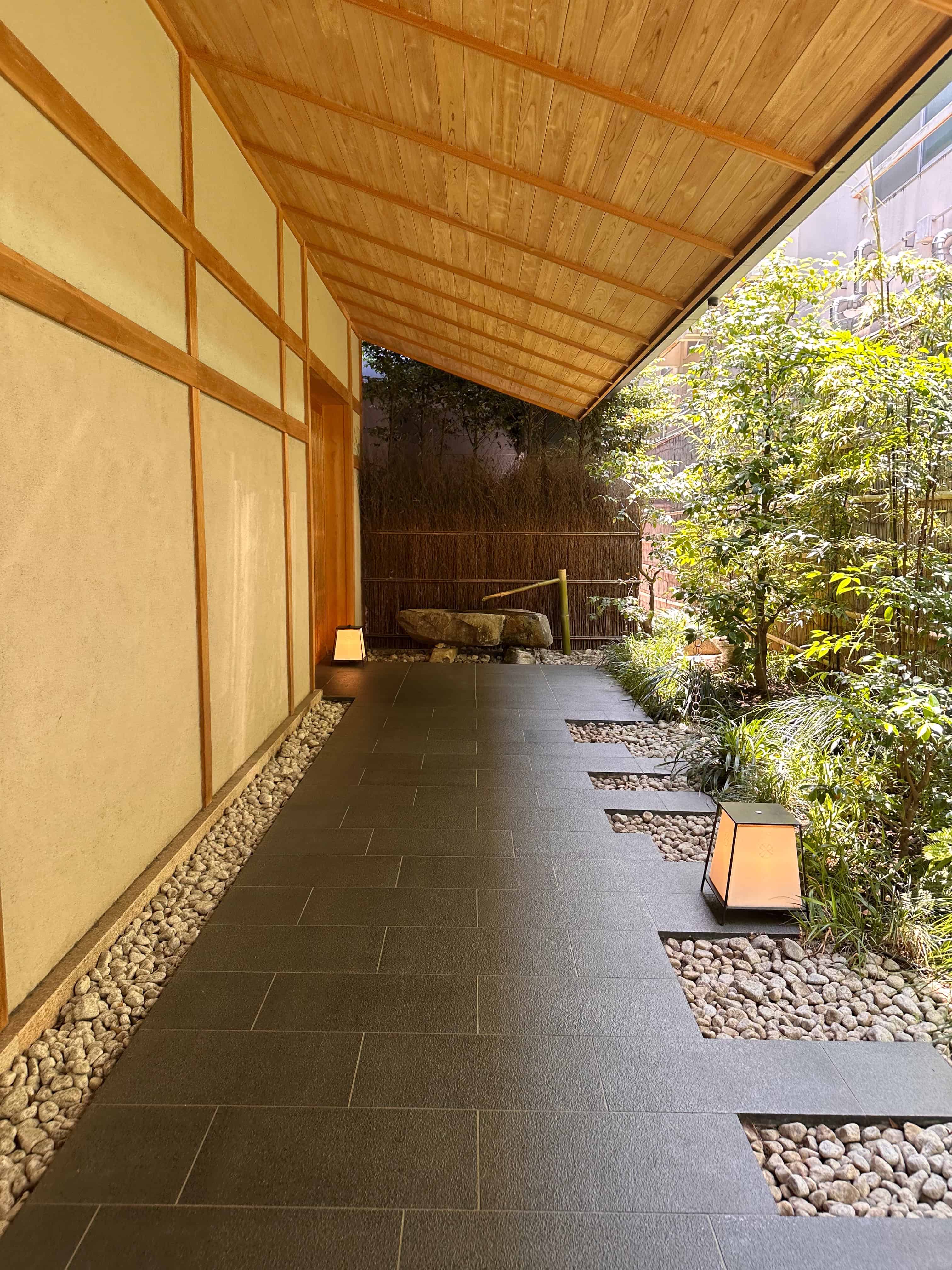 Entrance walkway at an Onsen Ryokan Hotel in Tokyo, featuring a covered wooden corridor, stone path, and landscaped garden.
